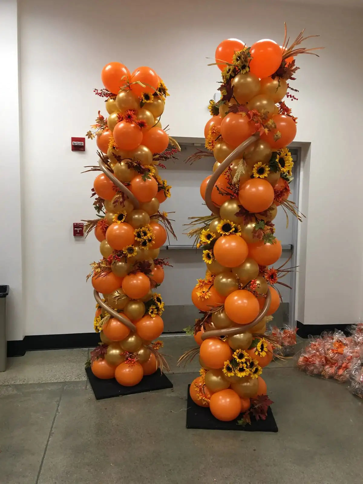 balloon columns orange and gold with sunflowers, fall colored leaves and gold twistee balloons garnishments 