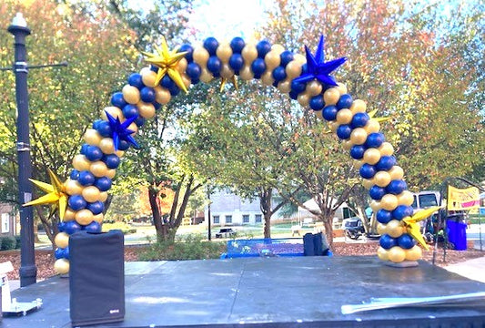 Blue and Gold Classic balloon arch on stage with blue and gold foil starburst balloon accents