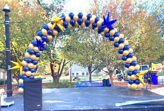 Blue and Gold Classic balloon arch on stage with blue and gold foil starburst balloon accents
