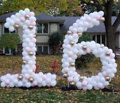 a set of large sculpted balloon numbers 1 and number 6 made with white and gold balloons on a lawn in a yard.