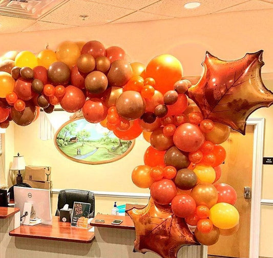a balloon garland arch with orange, yellow, brown and gold balloons accent with big foil balloon leaves