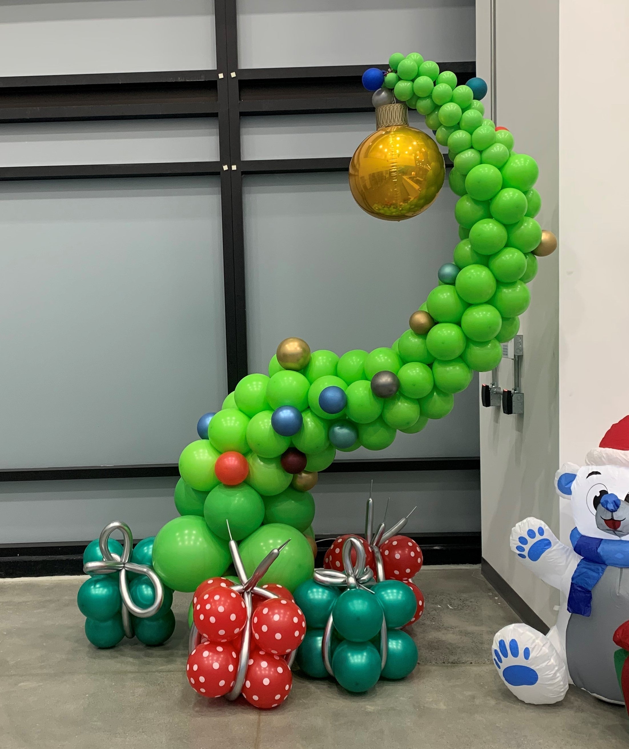 A balloon Christmas Grinch tree.  Curved with gold ornament on top with balloon presents on the floor.