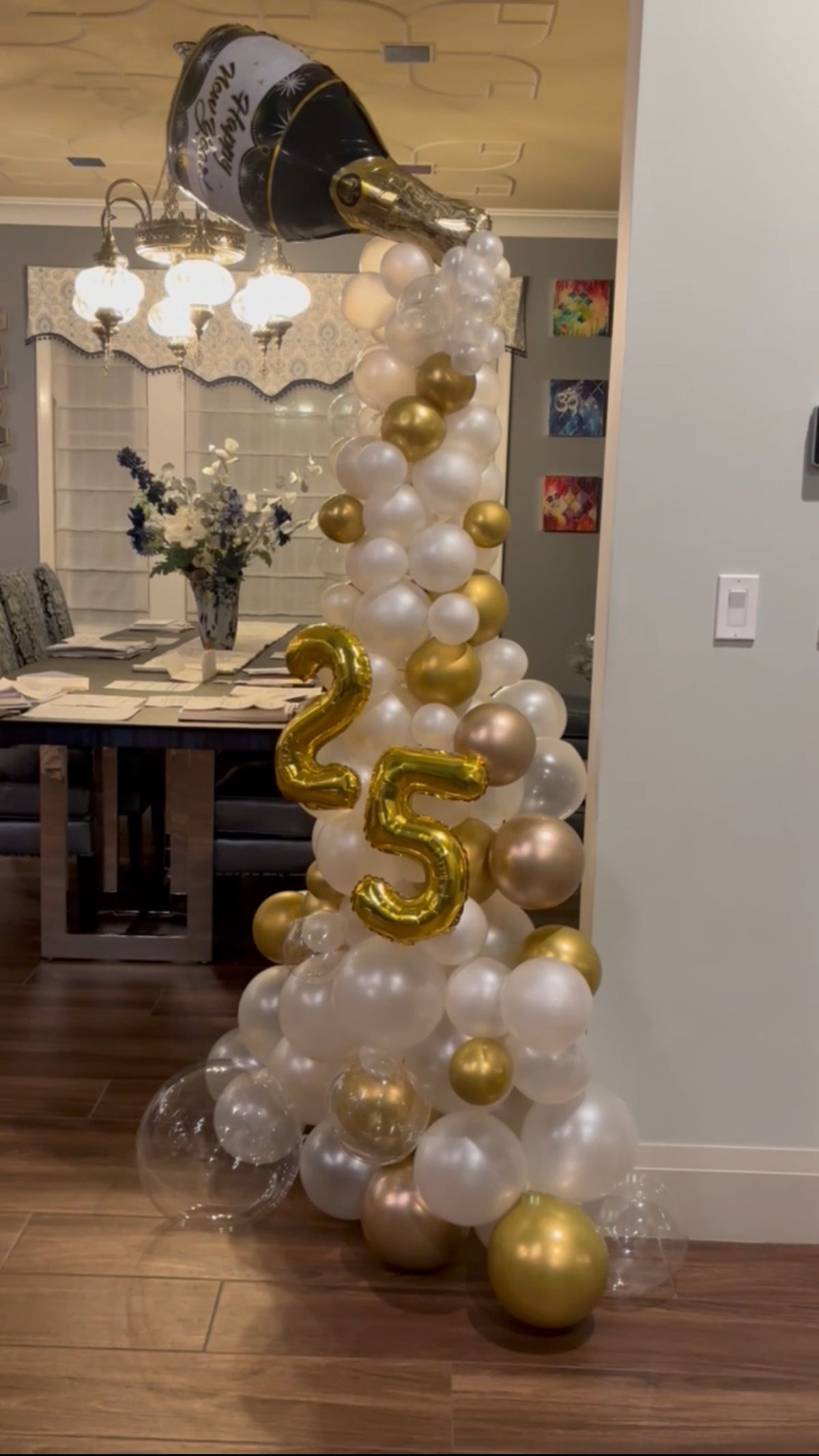 a balloon column with white, gold and clear balloons with champagne balloon on top.  a gold number 25 balloon is in front. 