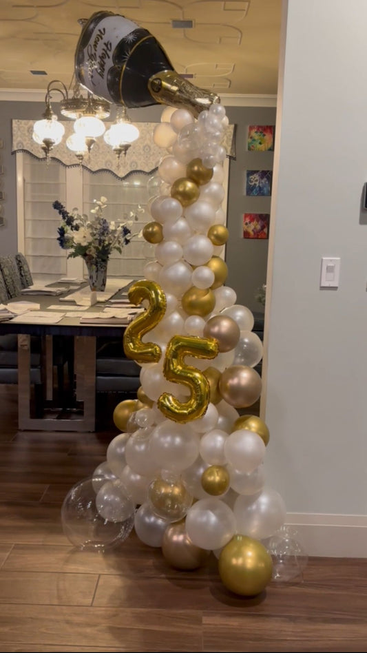 a balloon column with white, gold and clear balloons with champagne balloon on top.  a gold number 25 balloon is in front. 