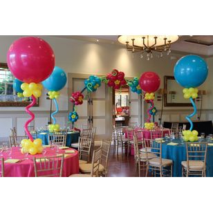 Large balloons on table tops red with yellow accent balloon and large jumbo blue balloons with accents connected with curly balloons on tables.