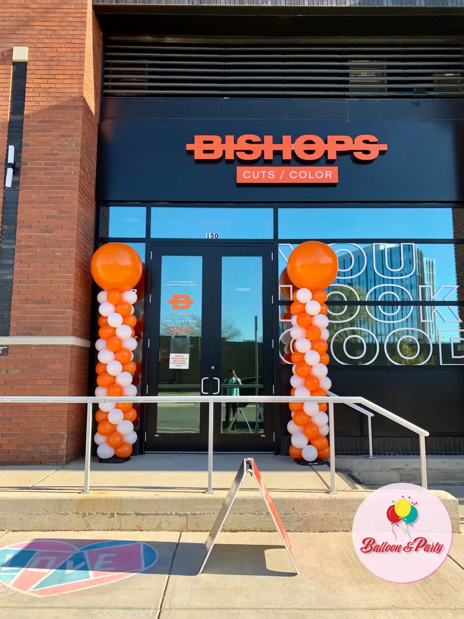 Orange and white balloon columns flank the entrance of a bishops salon.