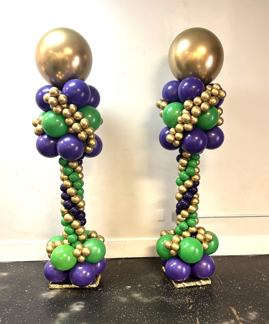 Two topiary balloon columns with gold, purple, and green balloons topped with chrome gold toppers.