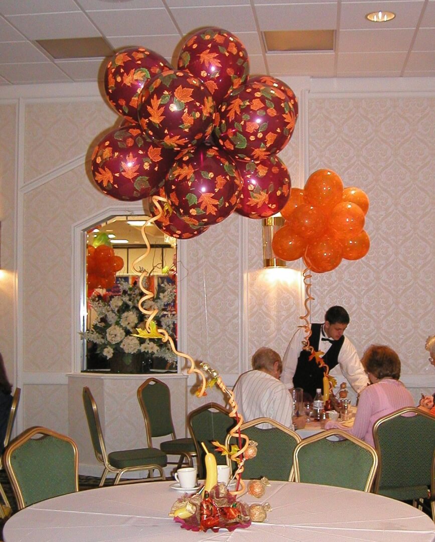 Thanksgiving themed centerpiece featuring fall leaves printed balloons in orange, yellow, and brown colors, displayed with a spiral stem on a stem