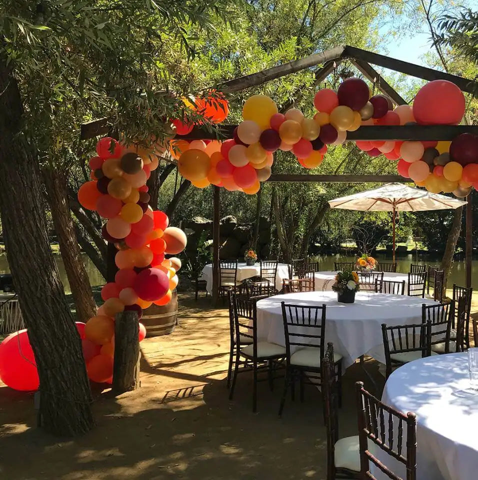 A vibrant archway of orange, red, and yellow balloons strung across a wooden frame.