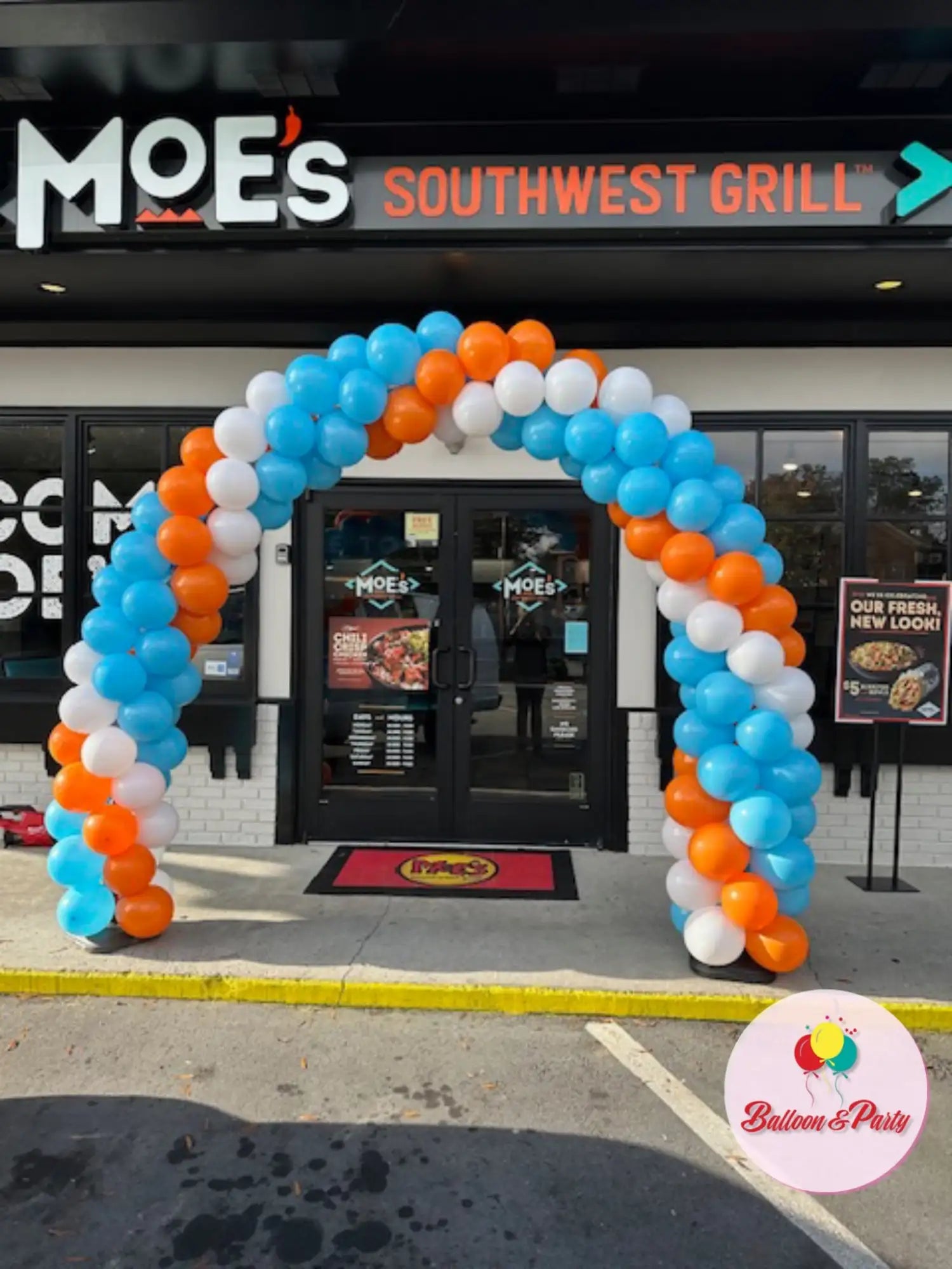 A vibrant balloon arch in shades of blue, orange, and white frames the entrance to moe’s southwest grill.