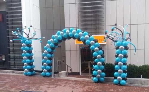 classic balloon arch silver, black and robin's egg blue and  matching columns with twistee balloons on top in front of hotel door