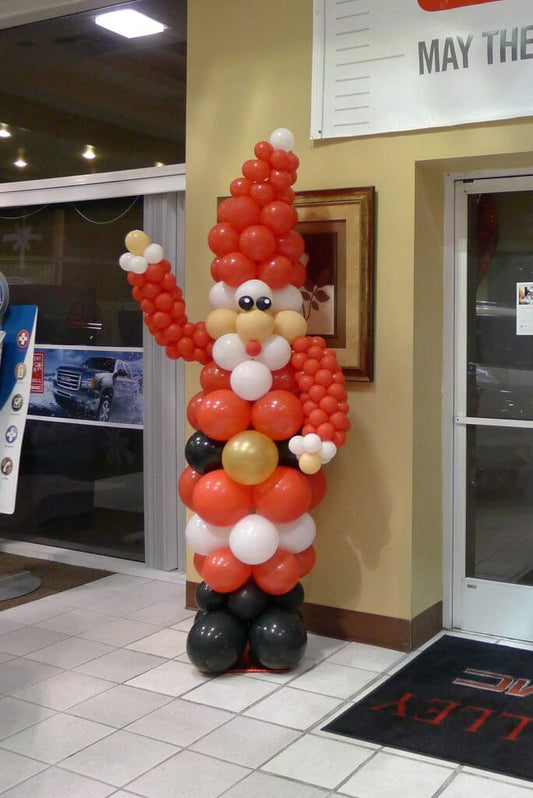 An 8-foot balloon sculpture of Santa Claus in traditional Santa colors of red, white, and black, standing inside a building.