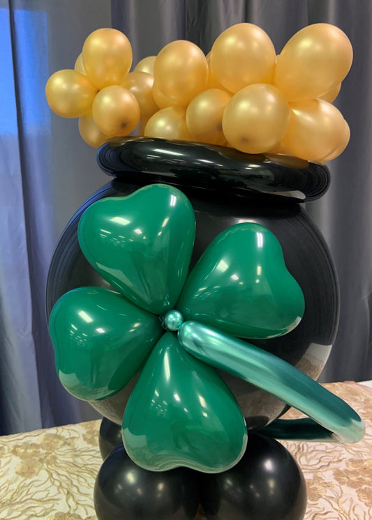 Pot of gold balloon sculpture with 4 leaf clover balloon sculpture in front and gold balloons on top.  Good St Patricks day party decorations.